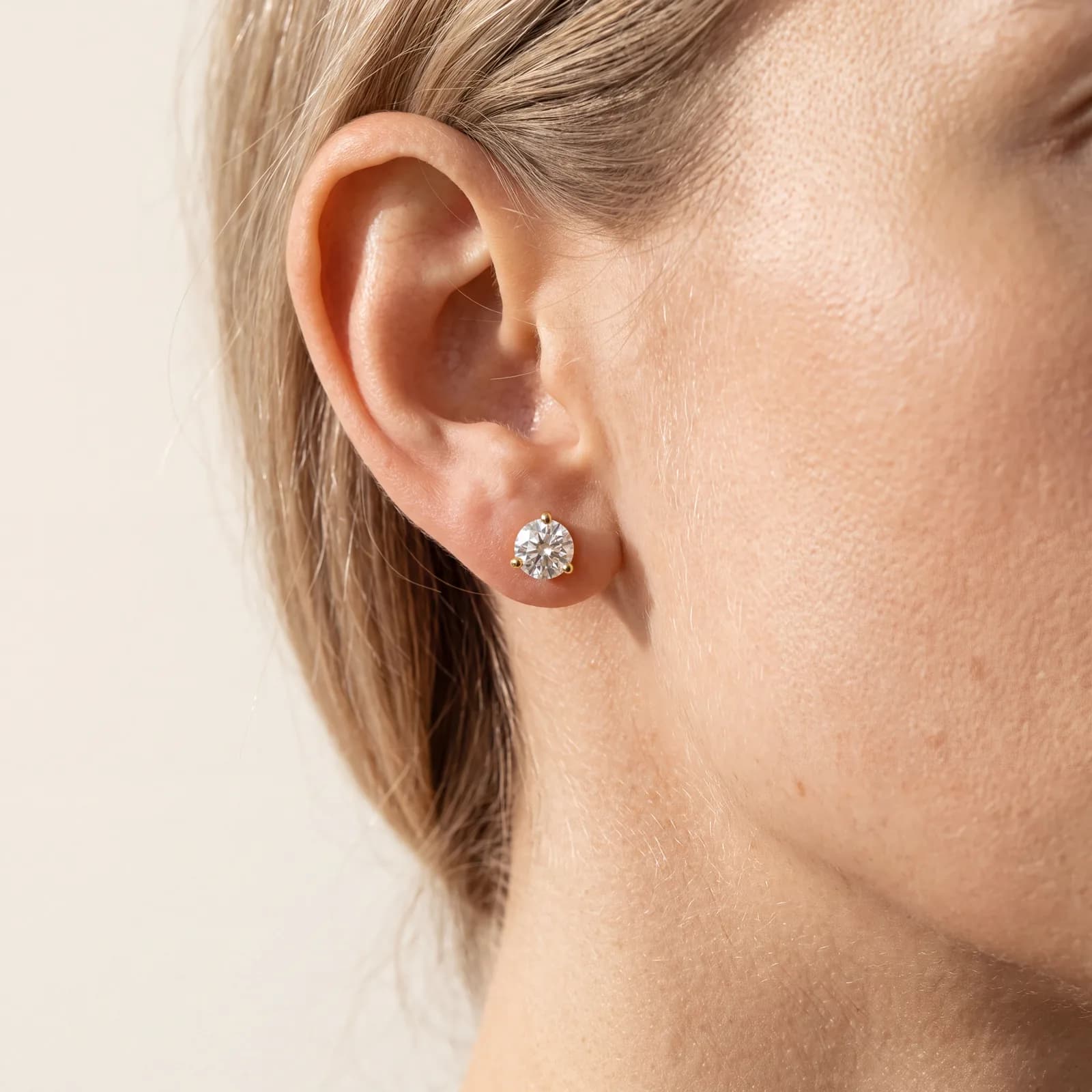 A close view of a blonde-haired ear and jaw wearing a round three-prong diamond stud earring.